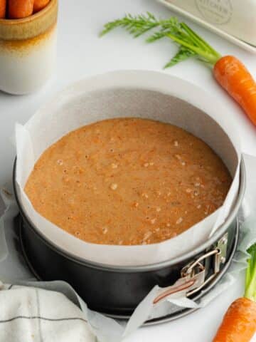 carrot cake batter in a parchment-lined cake pan before baking.
