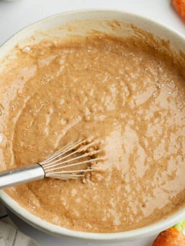 carrot cake batter in a large ceramic bowl with a whisk.