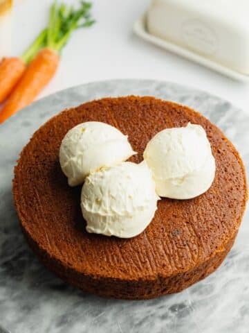 carrot cake with three scoops of frosting on top before being smoothed out.