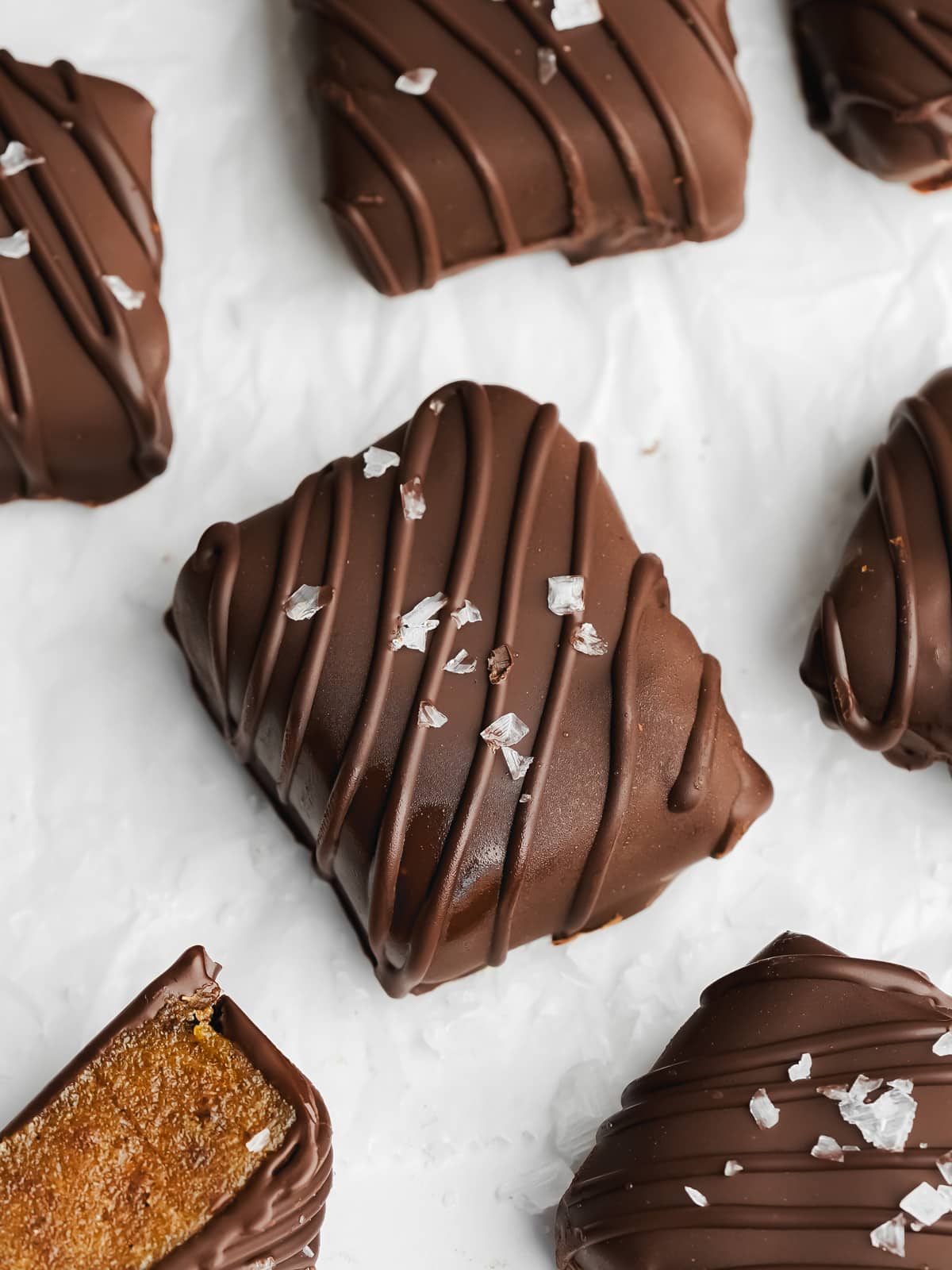 square chocolate caramels with flaky salt on a sheet of white parchment paper.