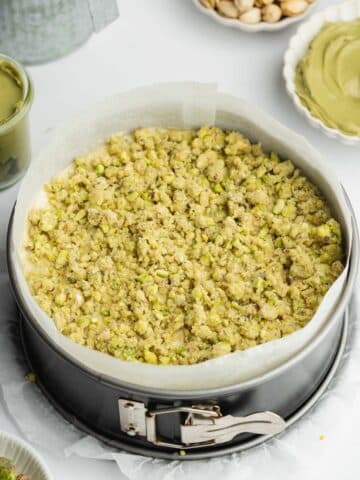 pistachio cake with green pistachio crumb topping in a lined cake pan before baking.