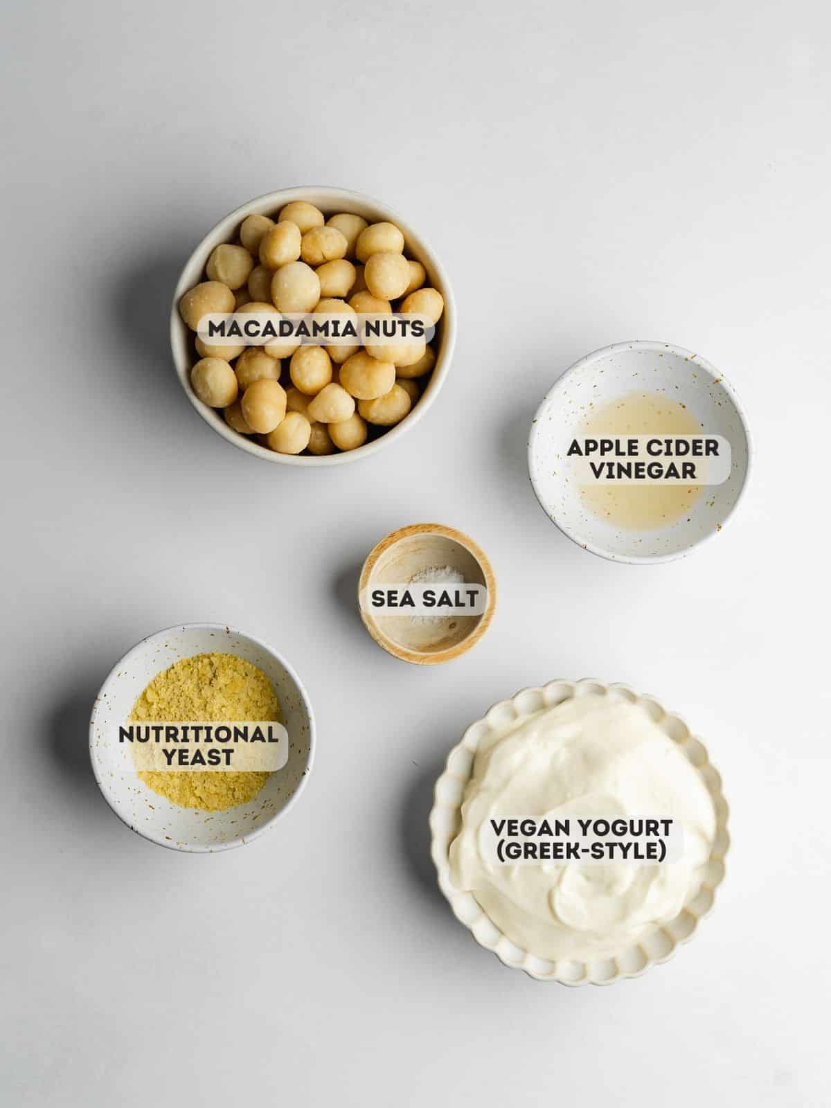 ingredients for macadamia cheese measured in bowls on a white surface.