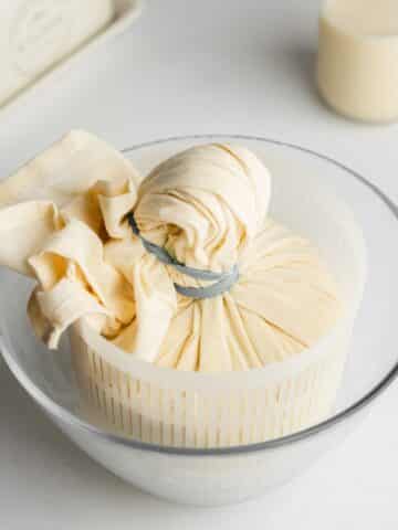 macadamia cheese wrapped in cheese cloth in a mesh bowl.