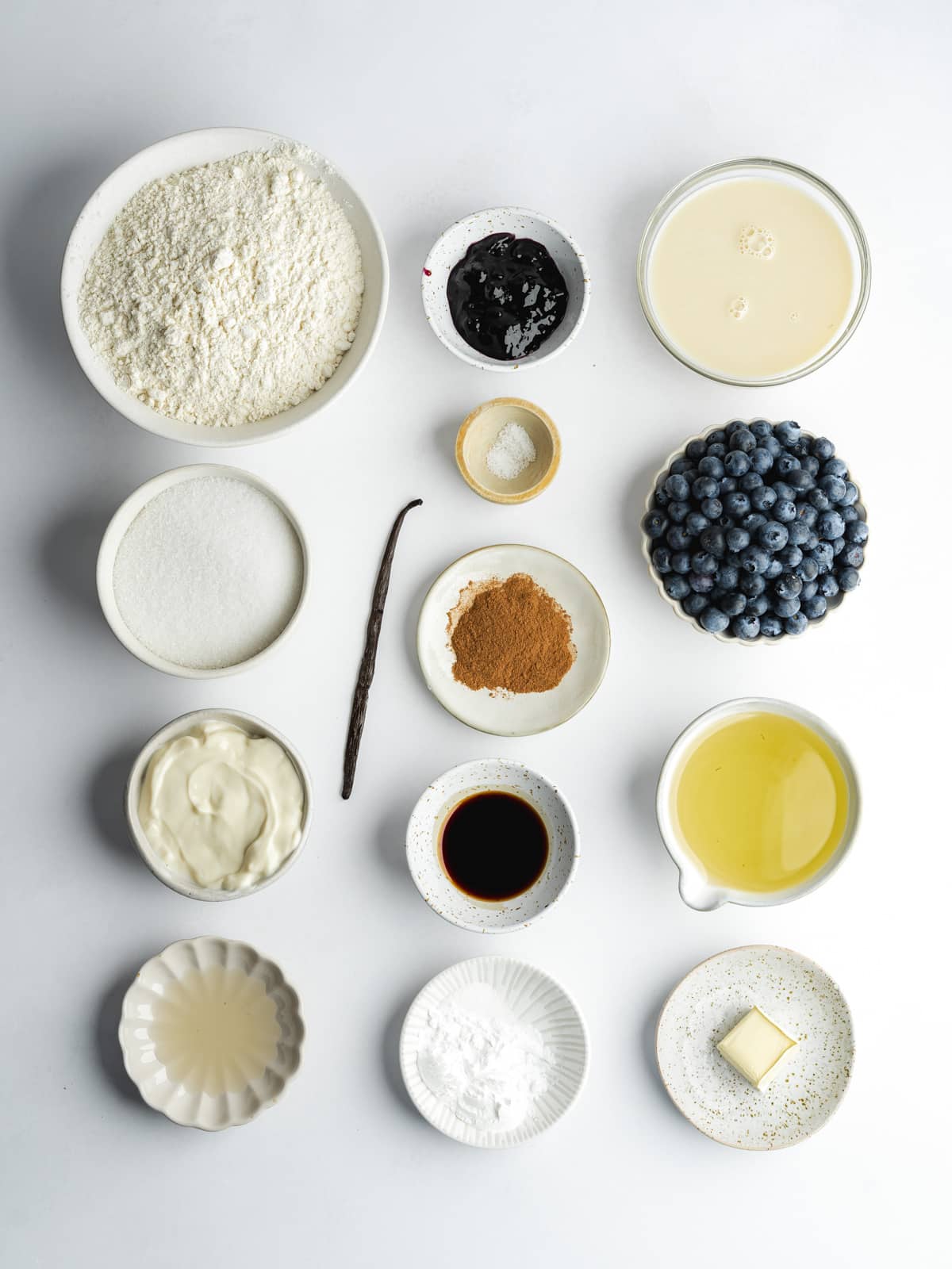ingredients for blueberry muffins measured out in bowls on a gray surface.