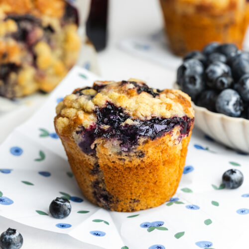 blueberry muffins on paper with fresh blueberries scattered around.