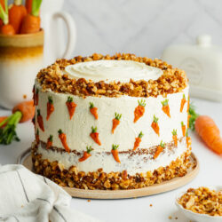 a carrot cake with piped carrot cake decorations and candied walnuts on top.
