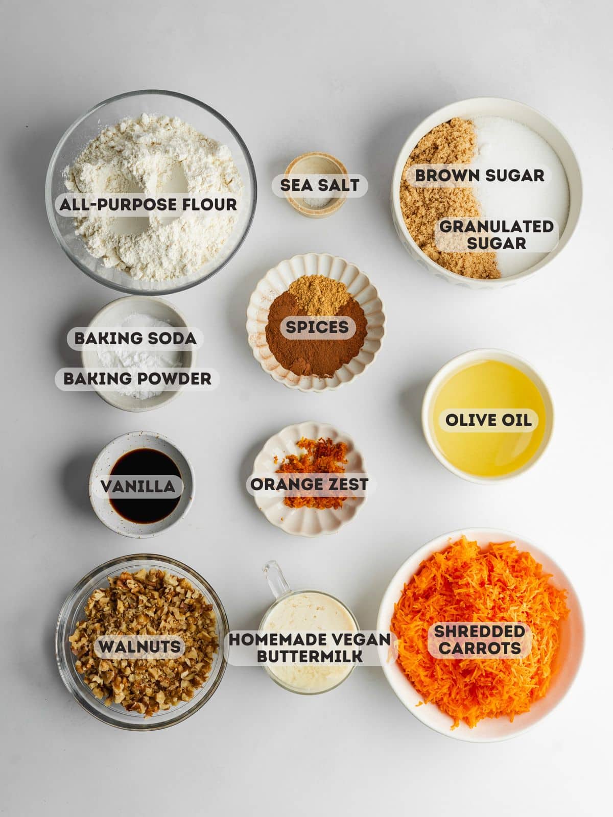 ingredients for carrot cake measured out in bowls on a gray surface.
