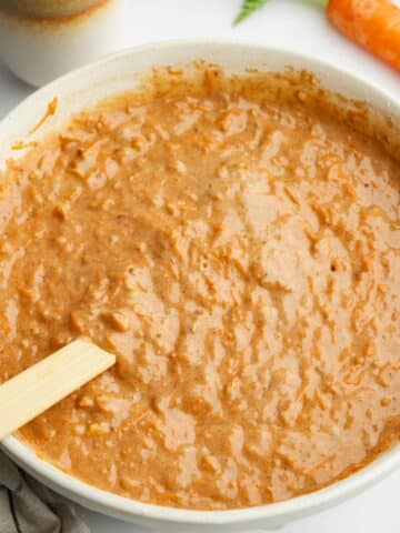 carrot cake batter in a bowl with freshly grated carrots and chopped walnuts folded through with a spatula.