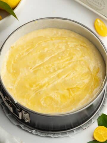 lemon cake in a springform pan with lemon curd swirled on top before baking.