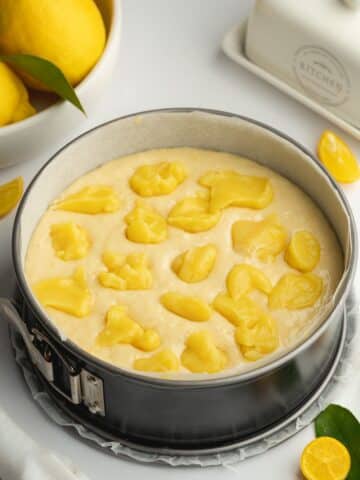 springform cake pan filled with lemon cake batter with dollops of lemon curd on top.