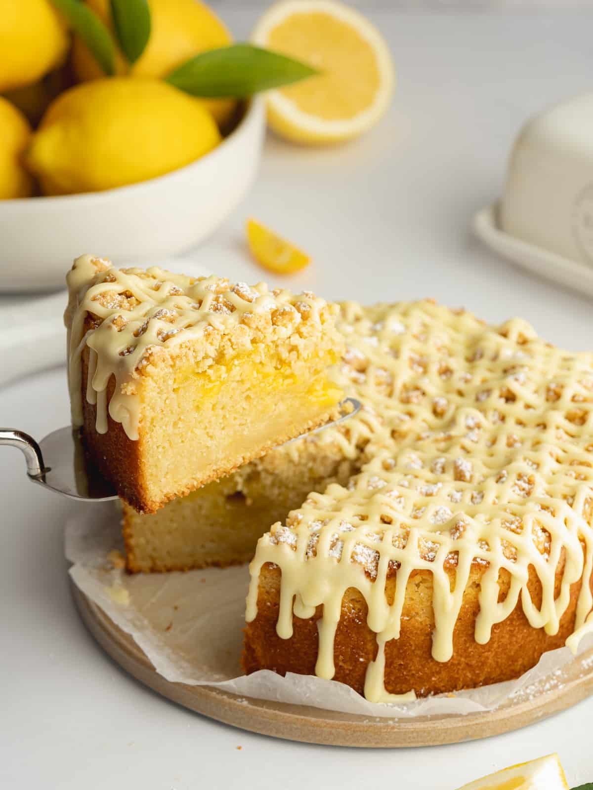 lemon cake with crumb topping and lemon icing and a slice being lifted away with a cake slice.