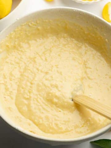 lemon cake batter in a ceramic mixing bowl with a rubber spatula.