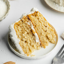 a slice of coconut cake on a white ceramic plate showing the moist and fluffy consistency.