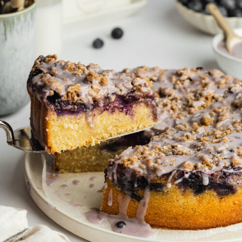 blueberry crumb cake with a slice being lifted away on a cake slice.
