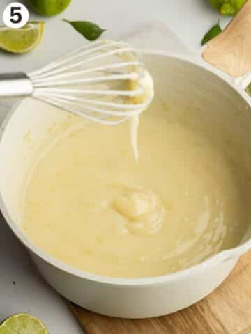 thickened key lime pie filling in a saucepan with a whisk drizzling it to show the consistency.
