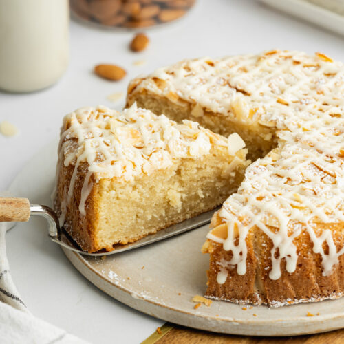 an almond flour cake on a ceramic plate with a slice being lifted away.
