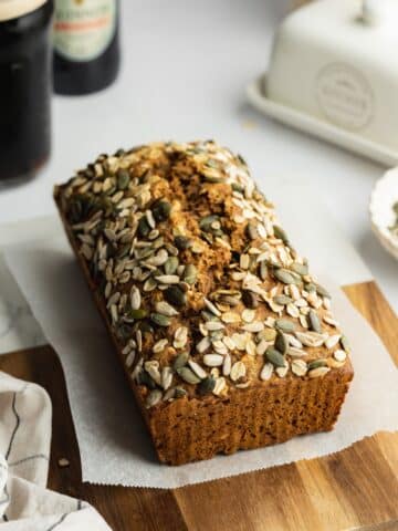 a freshly baked loaf of guinness bread topped with oats and seeds on a cutting board.