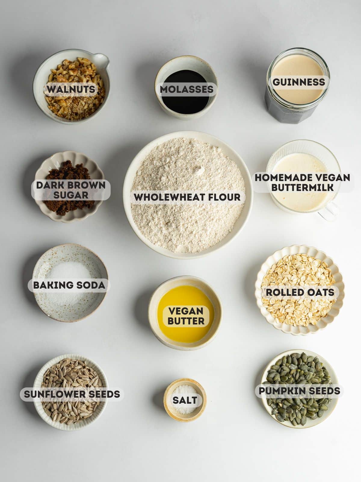 ingredients for vegan brown bread measured out in bowls on a gray table.