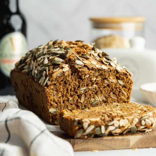 a loaf of guinness brown bread with a slice cut from it on a wooden board.