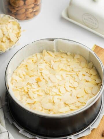 almond flour cake topped with flaked almonds in a lined cake pan before baking.