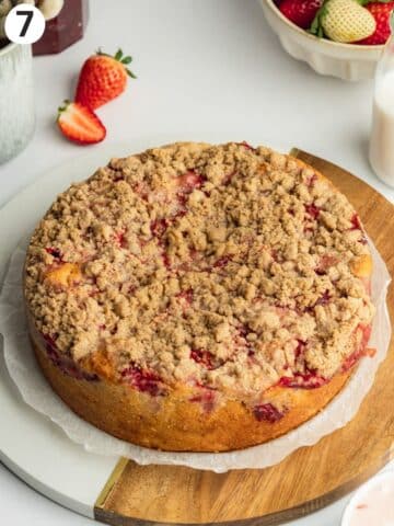 strawberry cake topped with crumble on a wooden cutting board.