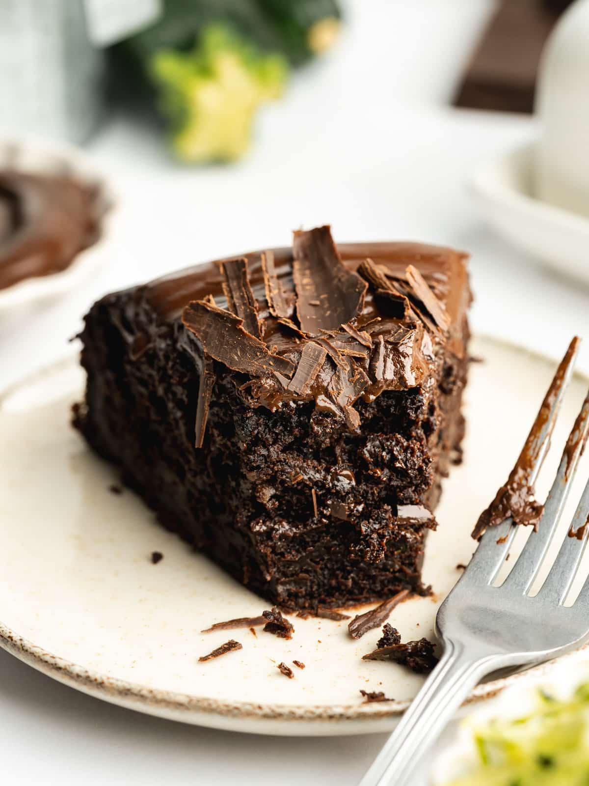 a slice of chocolate zucchini cake on a ceramic plate with a forkful taken from it showing the moist crumb consistency.
