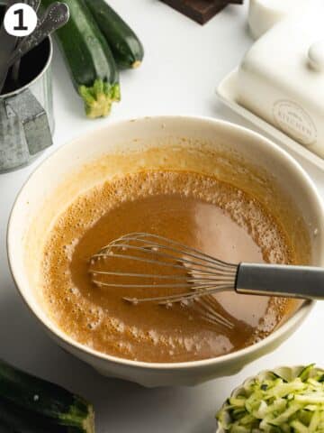 coconut sugar mixed with wet ingredients in a large ceramic bowl with a whisk.