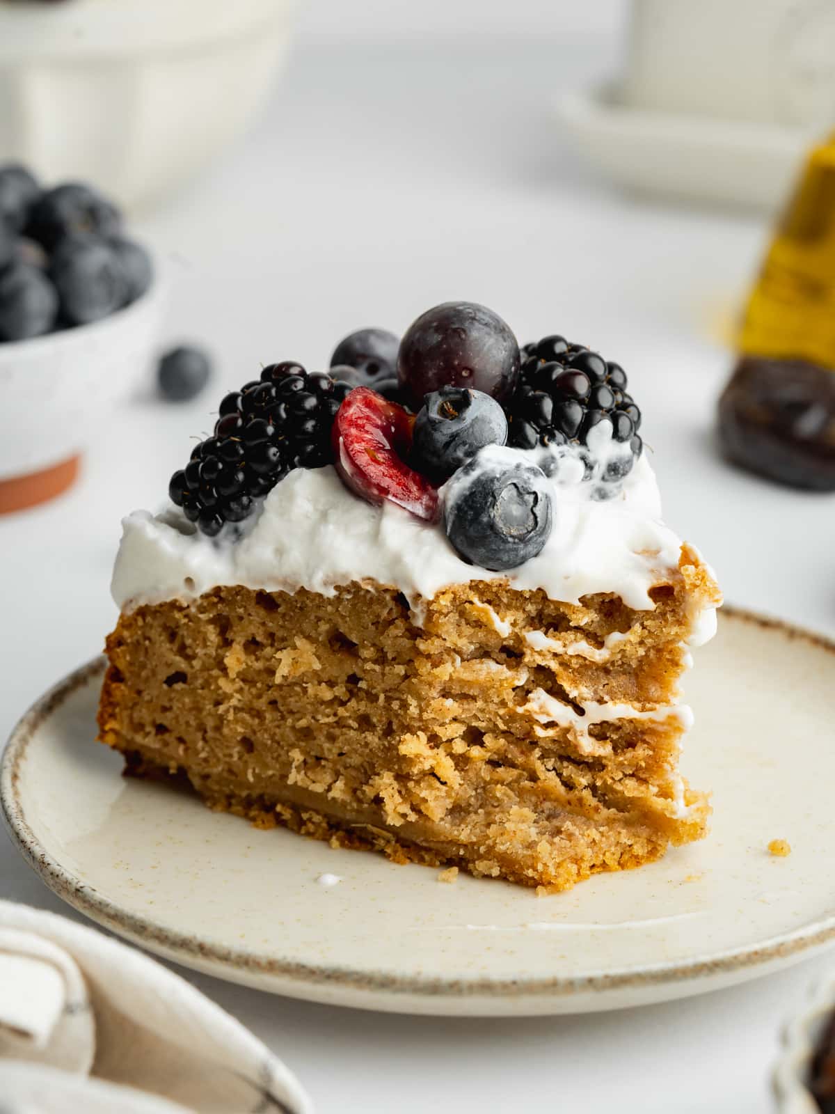 a slice of date cake with fresh berries and a forkful taken showing the moist texture.