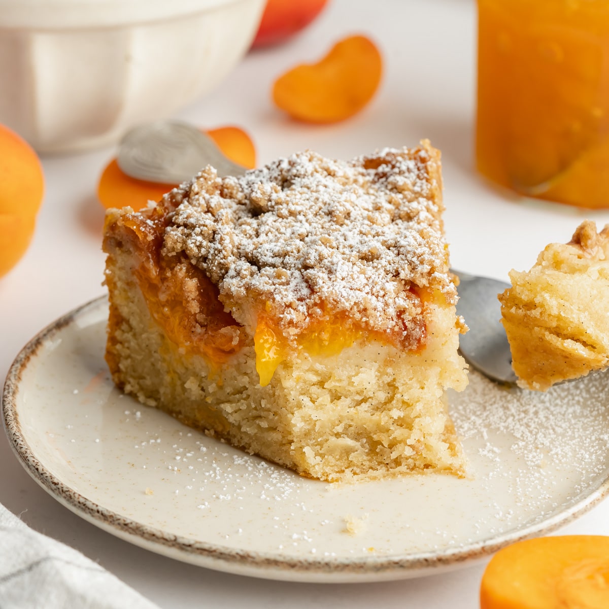 a slice of apricot cake on a ceramic plate with a dusting of powdered sugar.