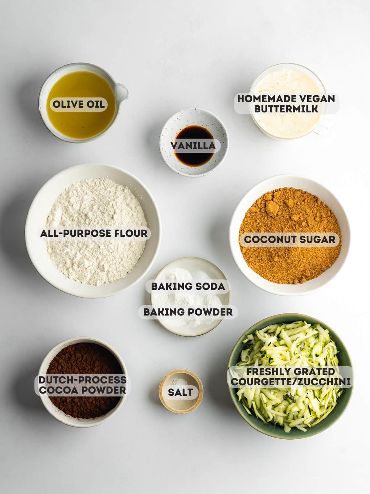 ingredients for chocolate courgette cake measured out in bowls on a gray surface.