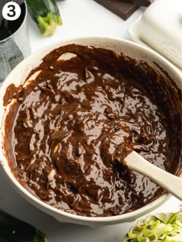 chocolate courgette cake batter being folded with a rubber spatula in a large ceramic bowl.