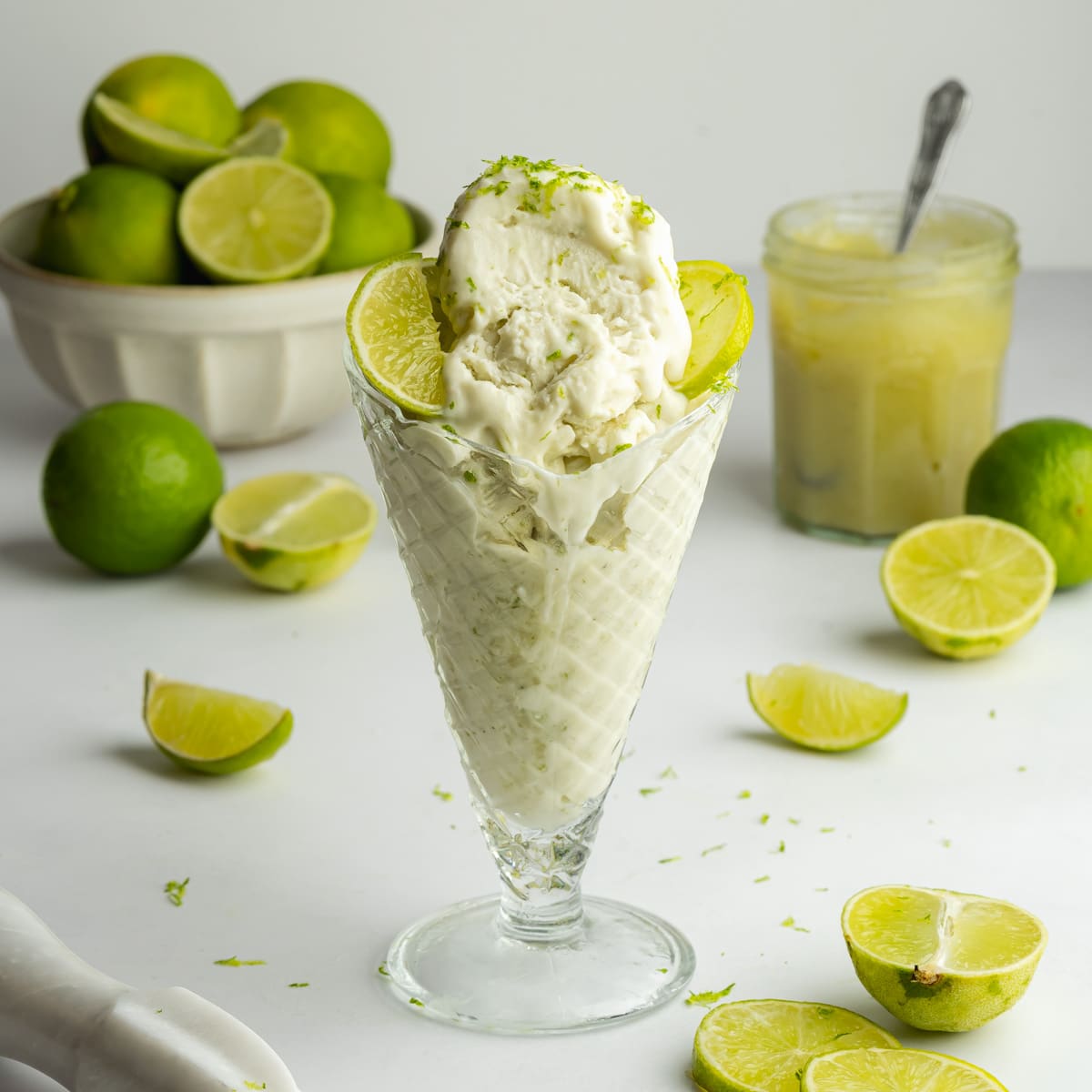 an ice cream glass filled with scoops of lime ice cream with fresh limes scattered around.