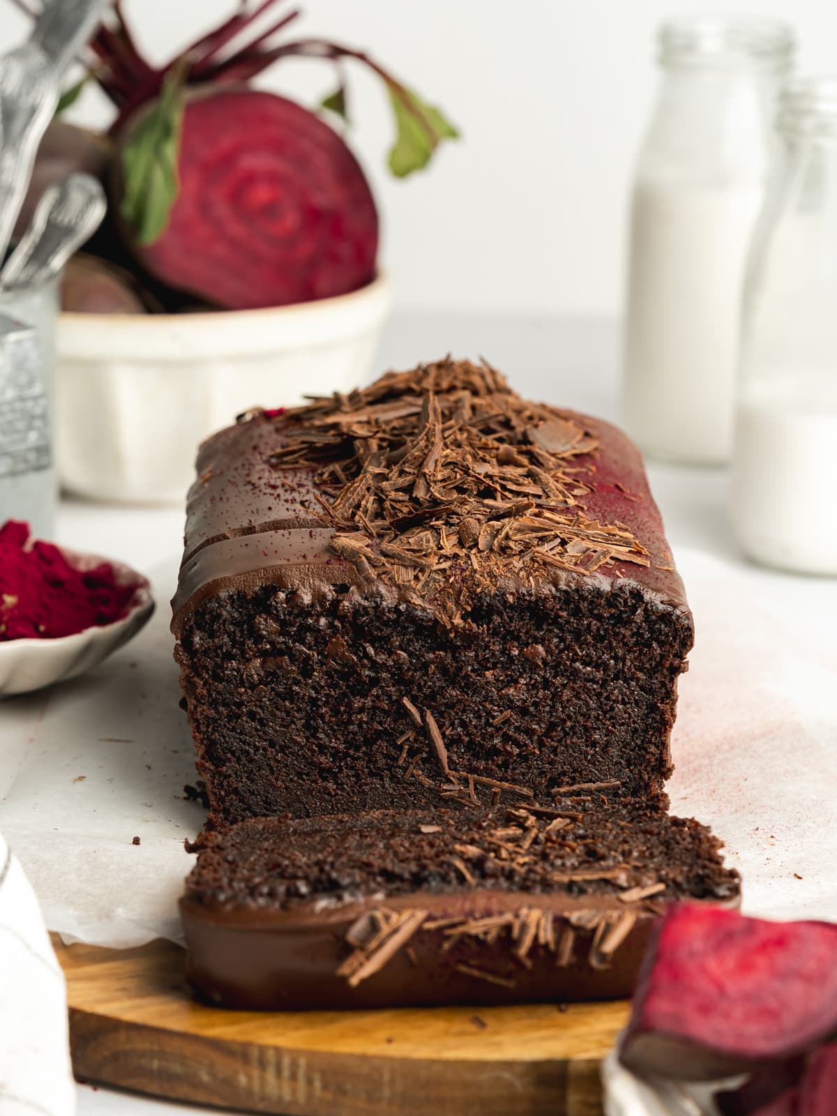chocolate beetroot loaf cake on a wooden board with a slice cut from it.