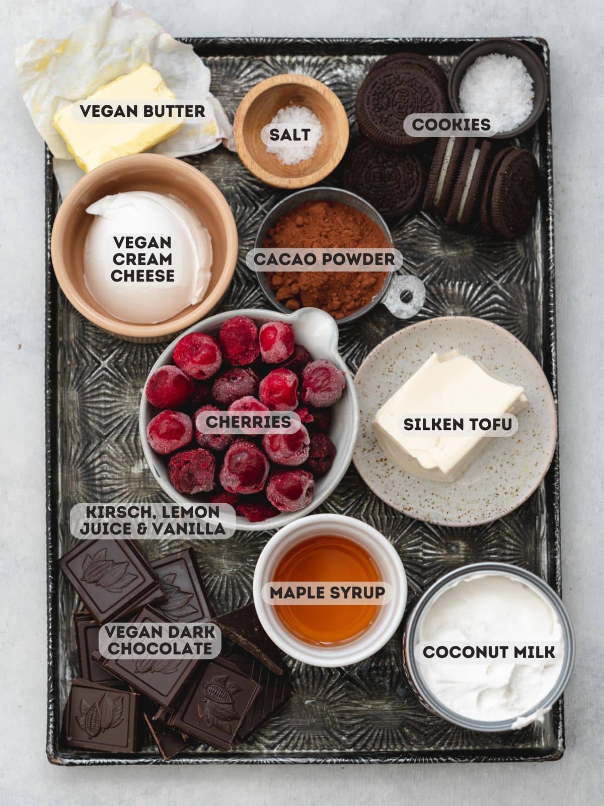 ingredients for vegan black forest cheesecake measured out in bowls on a metal tray.