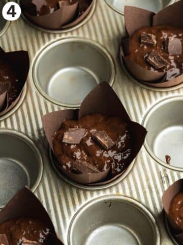 zucchini chocolate muffins with chocolate chunks on top in tulip liners in a muffin tray, with every second cavity left empty.