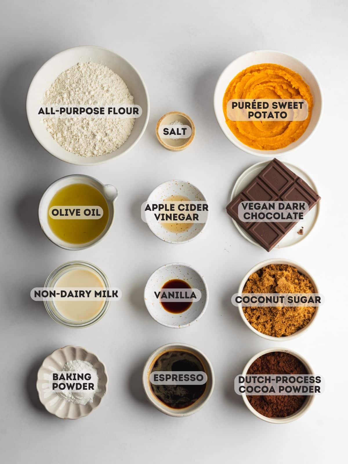 ingredients for chocolate sweet potato cake measured out in bowls on a light gray surface.