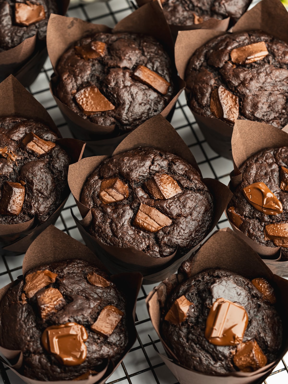 chocolate zucchini muffins on a wire rack with melty chocolate chunks on top.