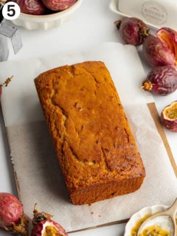 freshly baked passion fruit loaf on a cutting board with a sheet of parchment underneath.