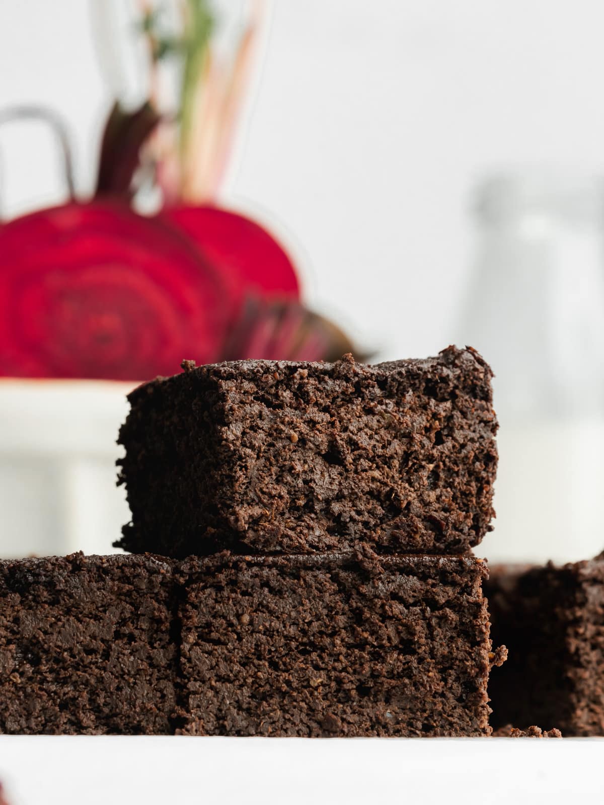 a stack of beetroot brownies with fresh beets in the background.