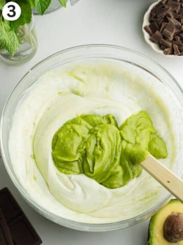 a bowl with whipped coconut cream and a spatula folding in blended avocado and condensed milk.