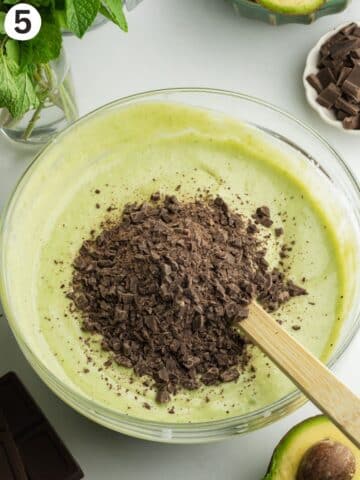 chopped dark chocolate added on top of a bowl of mint ice cream mixture before folding.