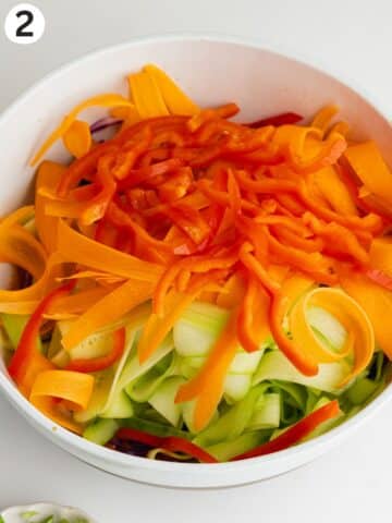chopped vegetables in a bowl on top of peanut dressing befores being tossed.