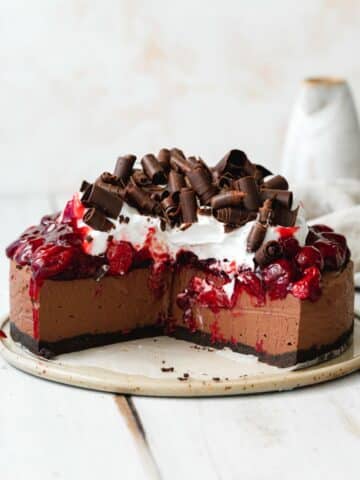 cherry chocolate cheesecake topped with chocolate curls and a few slices are taken from it.