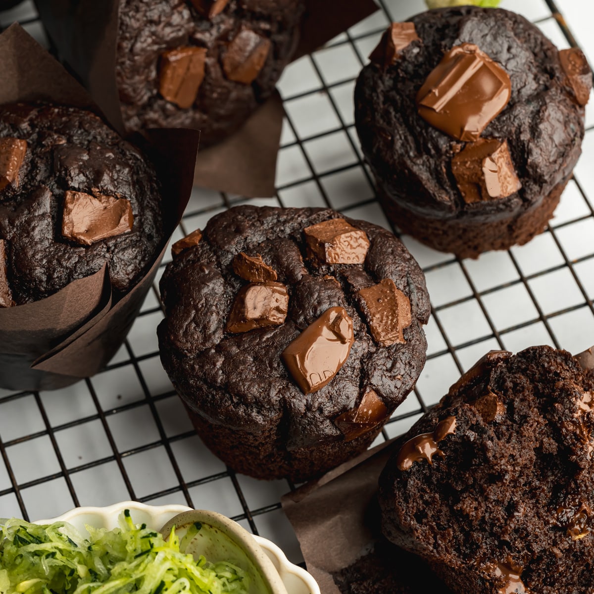 freshly baked chocolate zucchini muffins with melty chocolate pools on top of a wire rack.