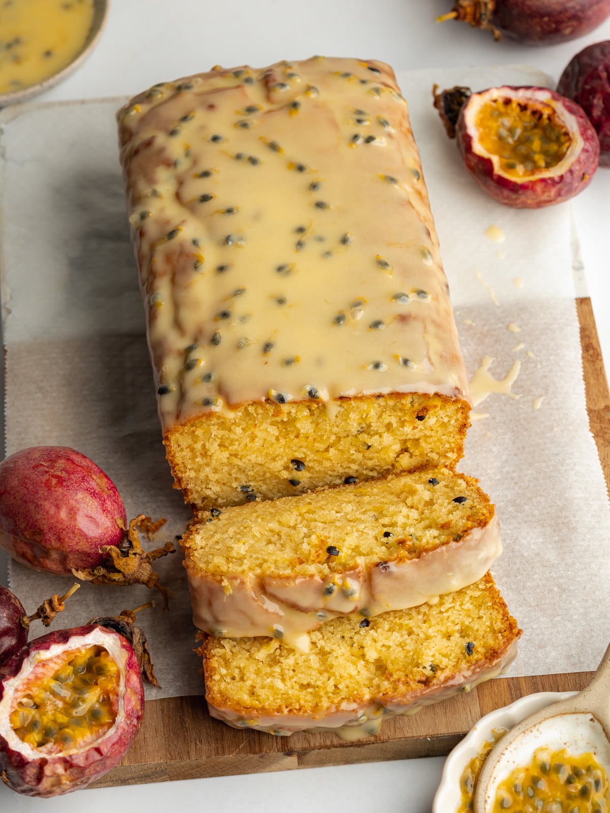 a glazed passion fruit loaf cake on a cutting board with a few slices cut showing the moist interior.