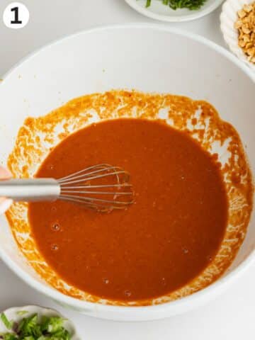 spicy peanut butter dressing in a large bowl with a whisk.