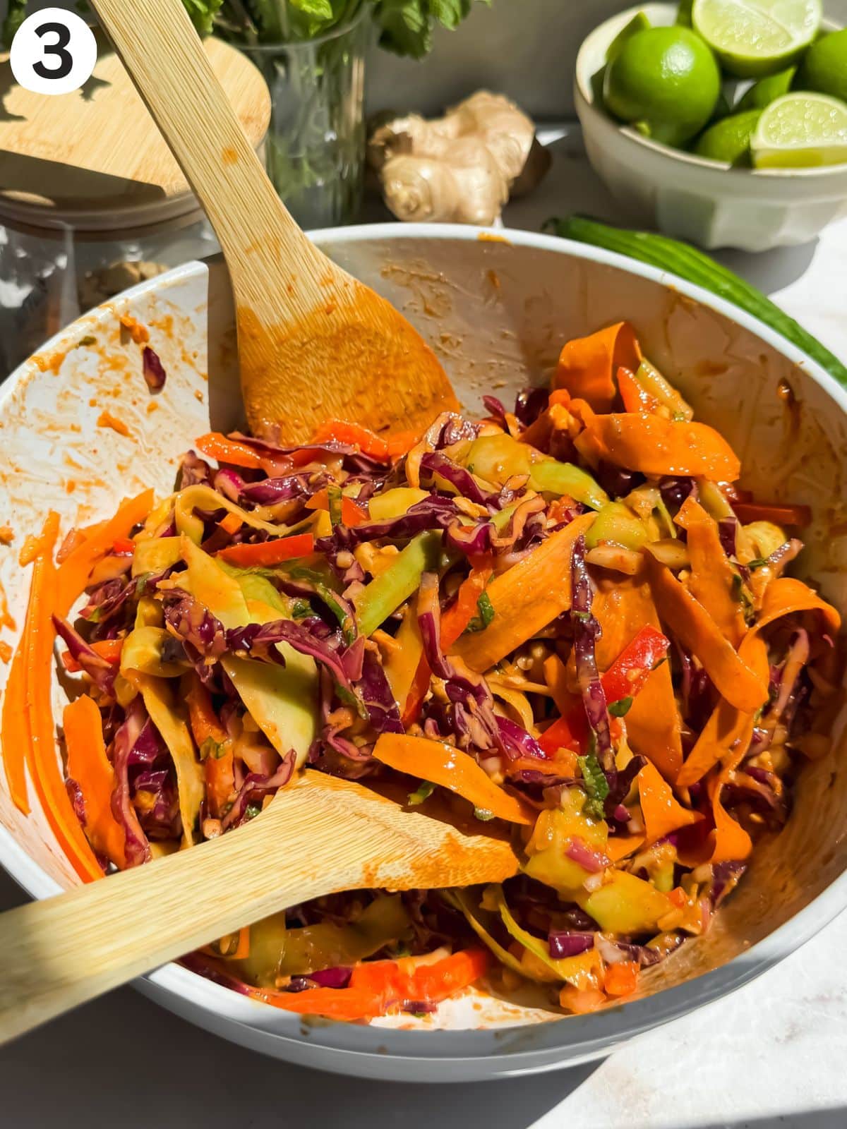 thai salad in a bowl with 2 wooden spoons for mixing.