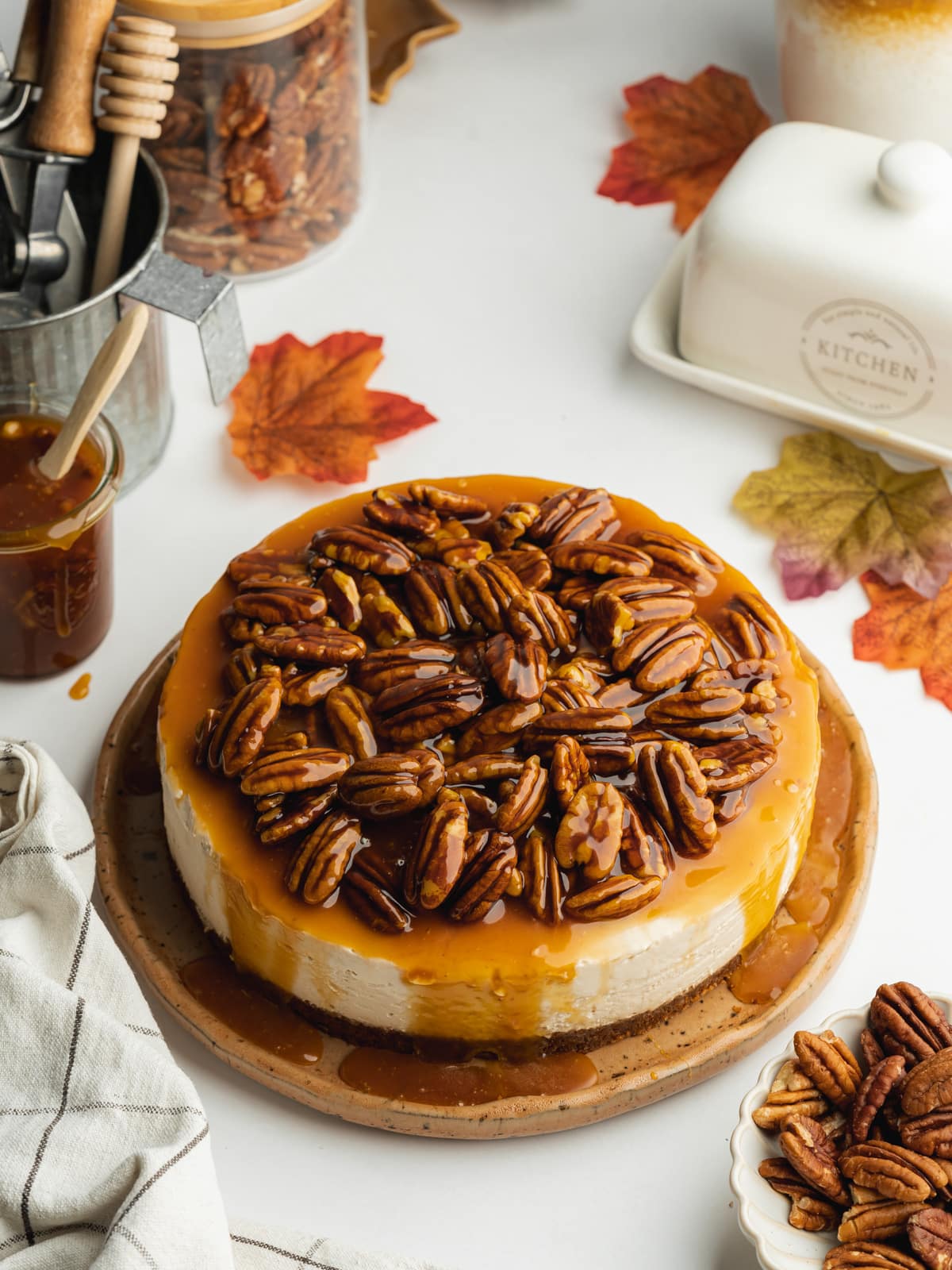 a pecan cheesecake topped with pecan caramel on a ceramic plate.