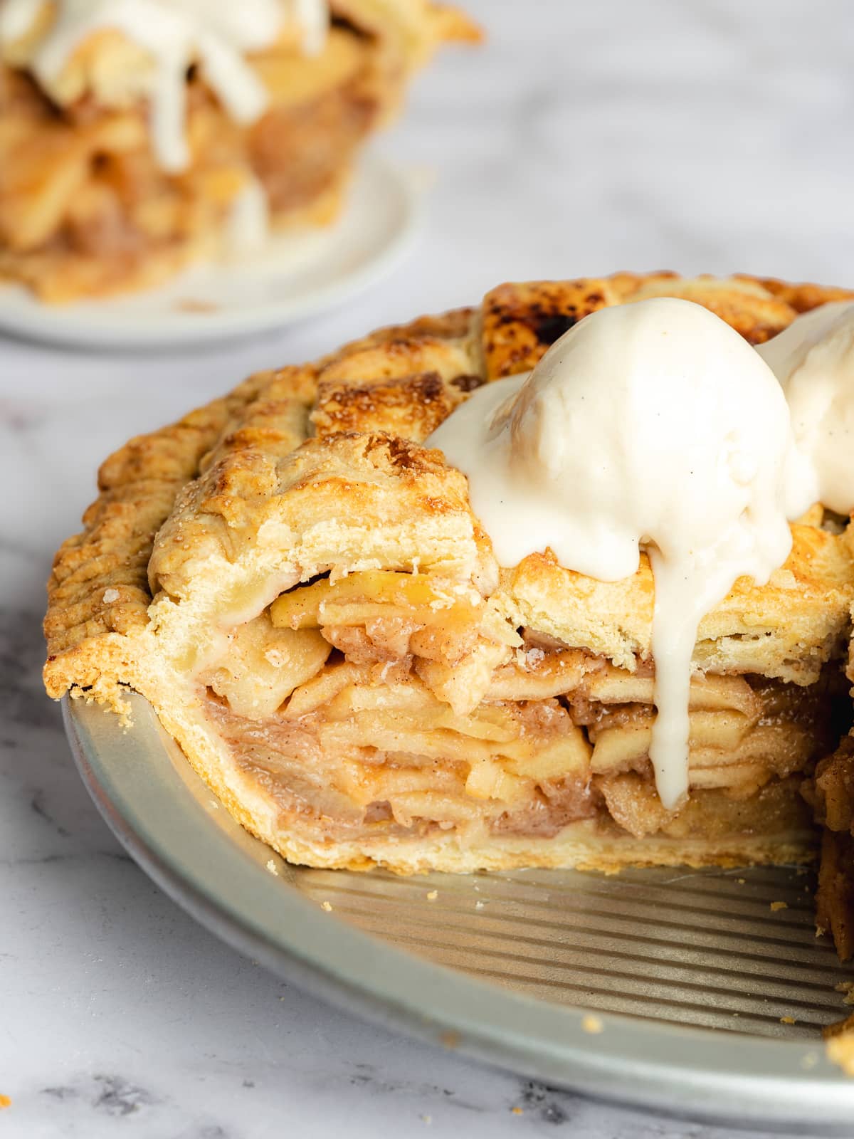 a deep dish apple pie showing the layered apple filling with melty vanilla ice cream on top.