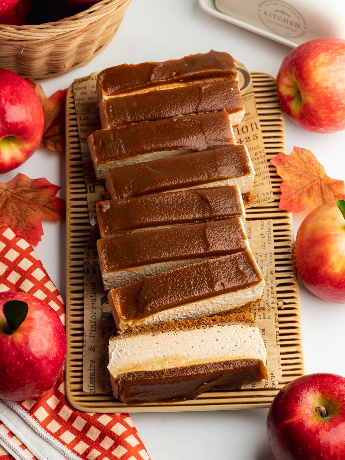 slices of apple cheesecake topped with apple butter with fresh apples scattered around.